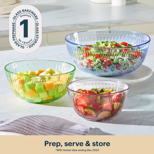 Three glass bowls filled with salad on a kitchen counter, featuring a brand logo in the corner.
