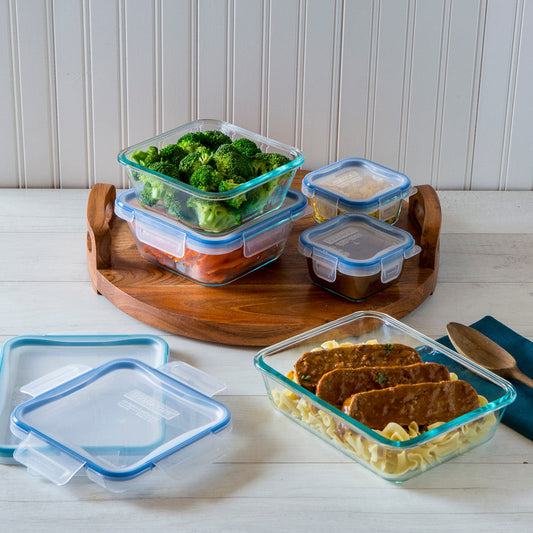 Glass food containers with lids on a wooden tray and white surface