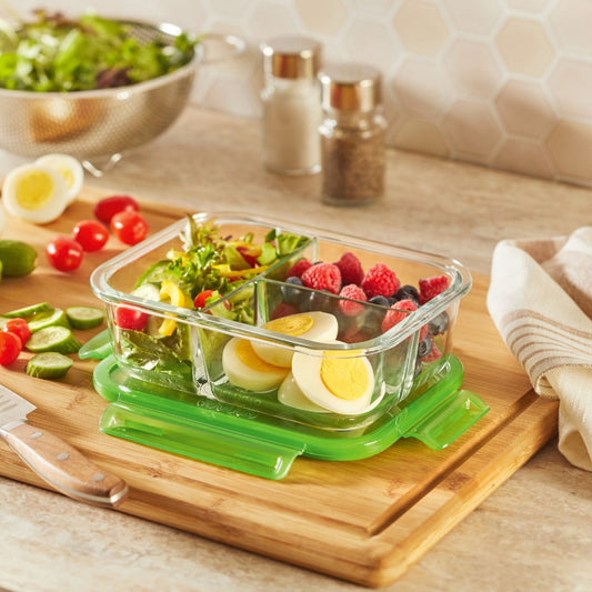 Glass food container with salad and hard-boiled eggs on a wooden cutting board with a kitchen background.